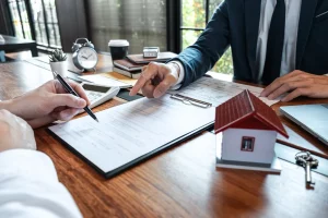 שני עורכי דין דנים בהסכם רכישת דירה עם מודל בית על שולחן העבודה